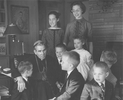 Archbishop Fulton J. Sheen seated with a group of children and teenagers