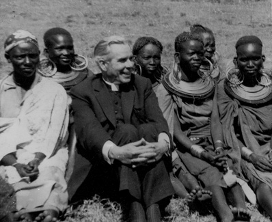Archbishop Fulton J. Sheen sitting outdoors with African women in traditional dress